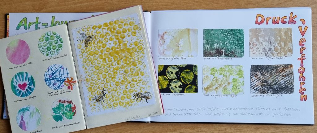 Das Bild zeigt zwei Skizzenbücher mit Beispielen für Materialdrucke. Die Druckproben sind im kleinen Buch rund im größeren Buch  rechteckig ausgeschnitten, aufgeklebt und mit Bleistift beschriftet worden.